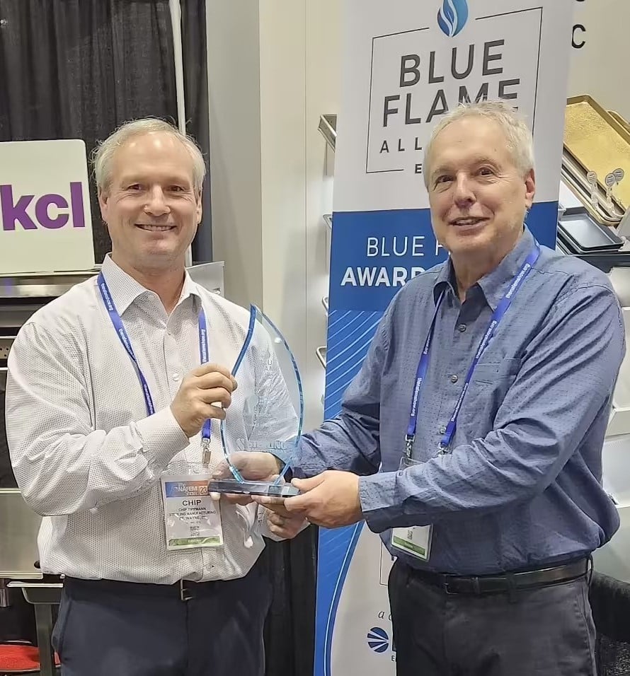 One person giving award to another person with blue flame logos and signs behind